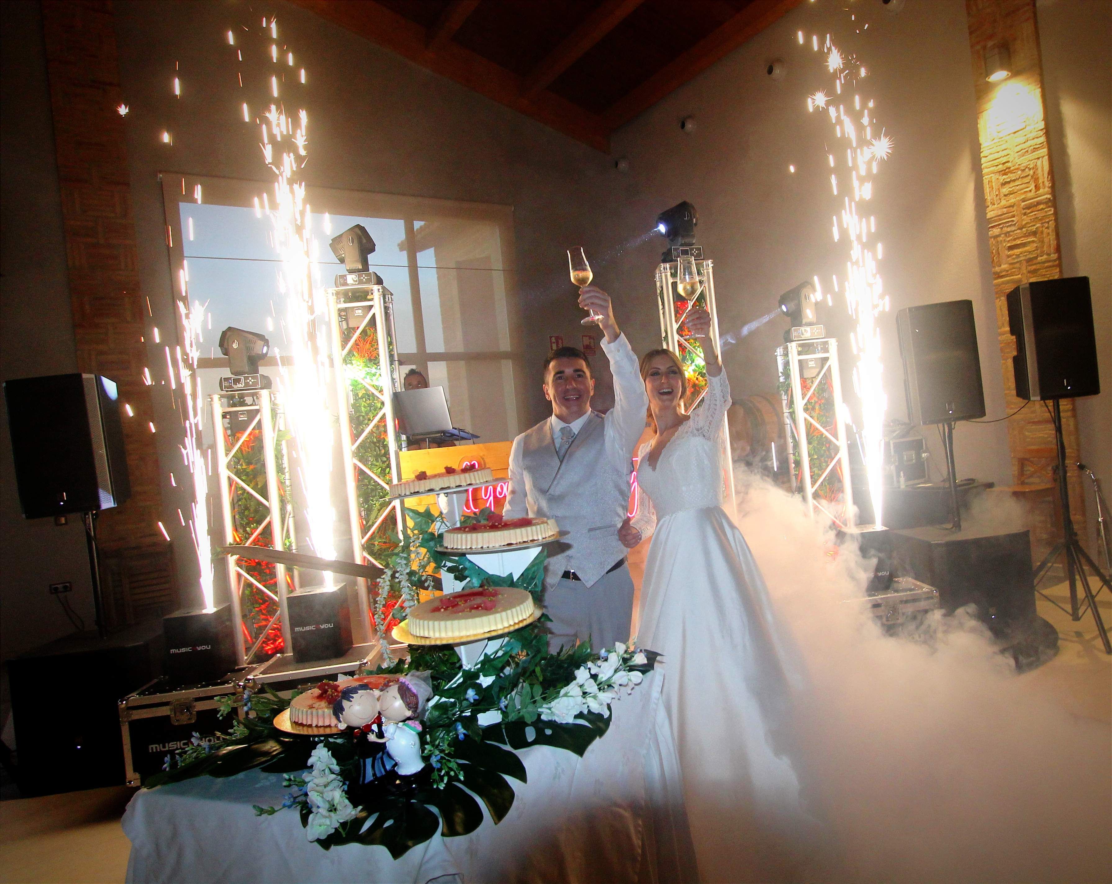 Una pareja corta el pastel de boda entre fuegos fríos y humo bajo