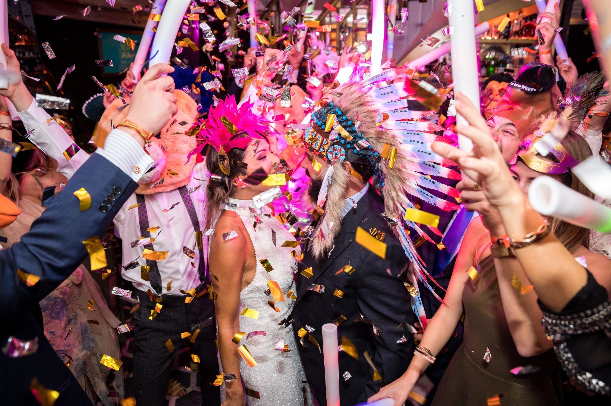 Invitados de una boda bailando con disfraces, plumas y confeti durante la Hora Salvaje