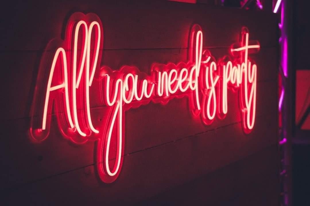 Rótulo de neón rojo «All you need is party» en una fiesta